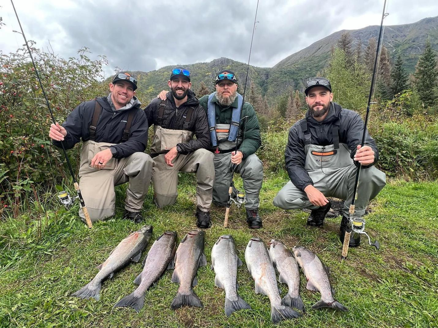 A group of people holding fishing rods and displaying their caught sockeye and silver salmon on the ground during a guided fishing trip on the Kenai River.